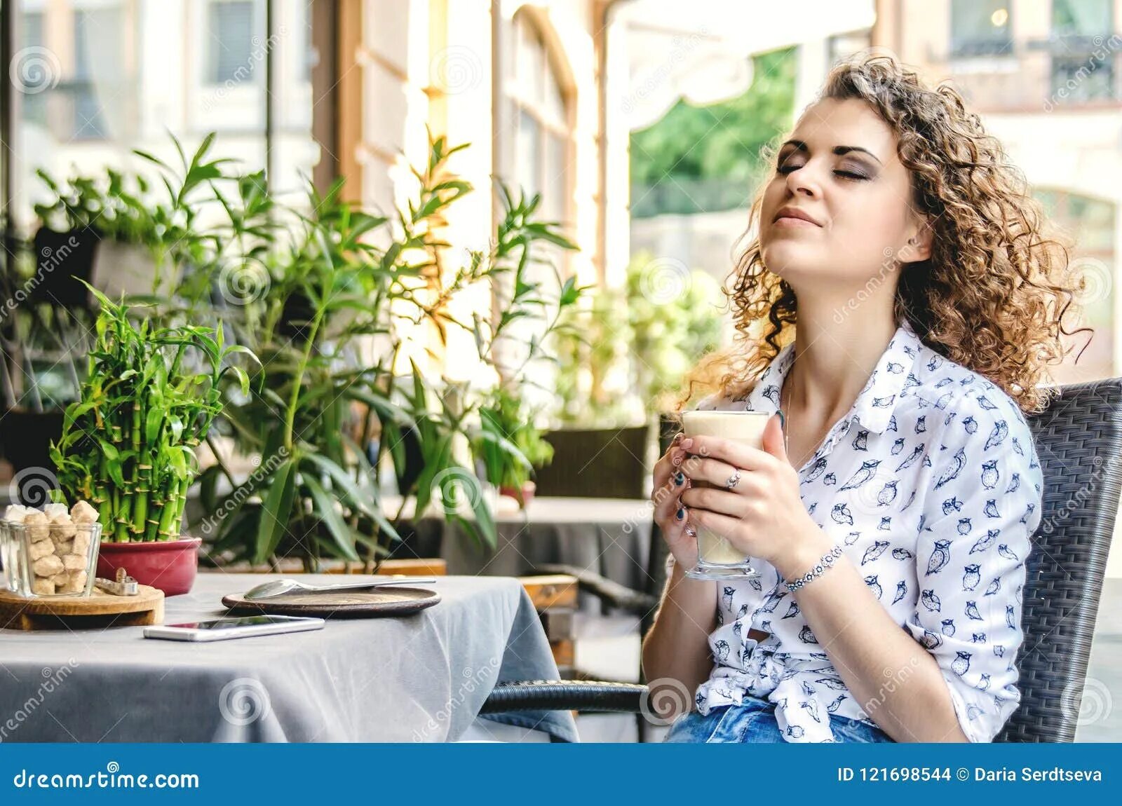 Кафе девушка фото кофе A Girl is Enjoying Coffee Sitting in a Cafe on the Summer Terrace. Stock Photo -