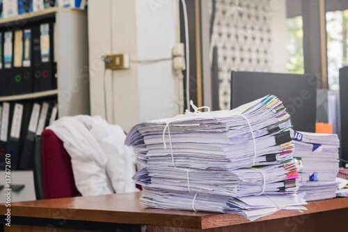 Куча бумаг на столе фото Pile of documents on desk stack up high waiting to be managed фотография Stock A