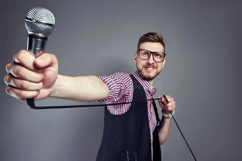 Поет парень в очках свои песни фото Karaoke Man Sings the Song To Microphone, Singer with Beard on Grey Background. 