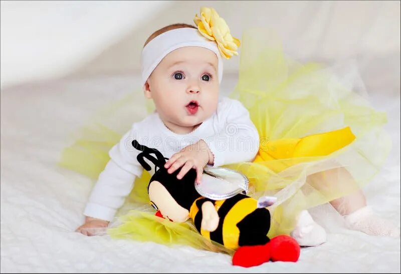 Покажи фото малыша в желтом A Small Child in a Yellow Skirt Sits on the Bed with a Toy Bee Stock Photo - Ima