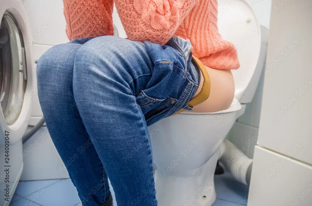 Попки в туалете фото A woman with constipation or diarrhea is sitting on the toilet in blue jeans on 