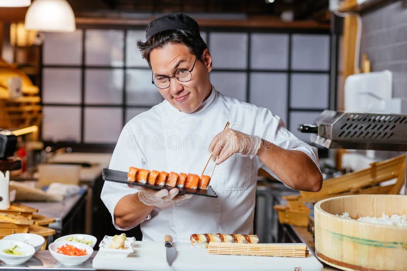 Повар суши фото Cunning Chef Wwinking To the Camera while Holding a Plate with Sushi Stock Image