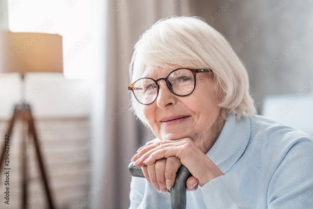 Пожилая женщина в очках фото Close up of mature woman in glasses holding cane while sitting on sofa at home ф