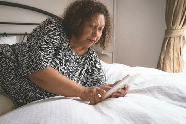 Пожилые женщины на кровати фото Senior woman using digital tablet on bed in bedroom at home - touchscreen, covid