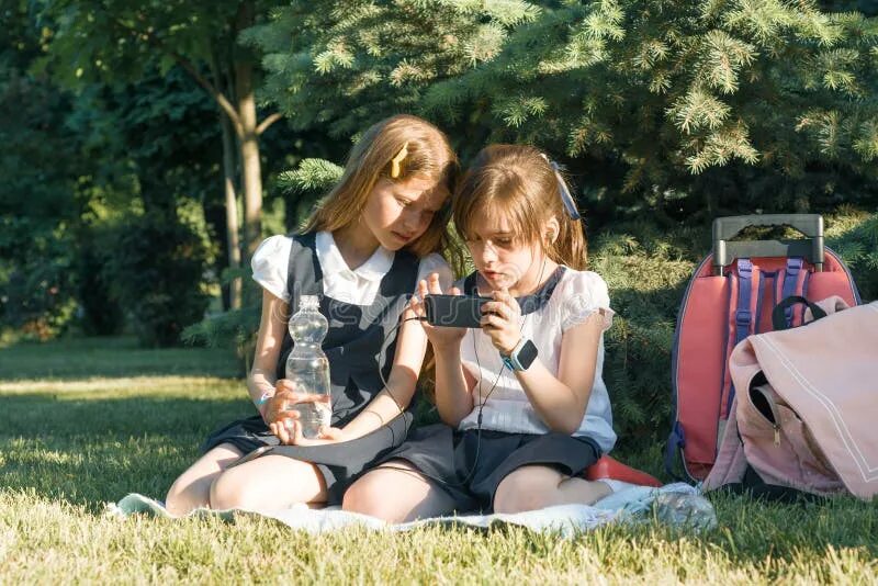 Природа школьницы фото Two Little Schoolgirls Using a Smartphone. Children Playing, Reading, Looking at