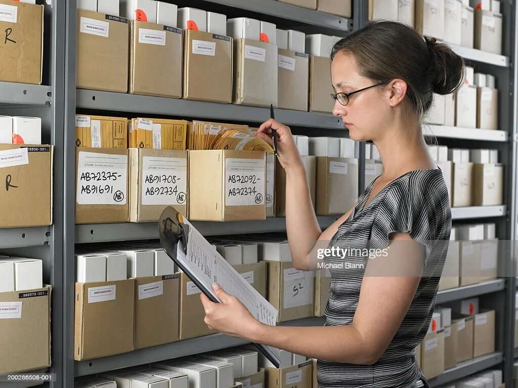 Работа в архиве фото Woman Holding Clipboard By Rows Of Boxes In Storage Room High-Res Stock Photo - 