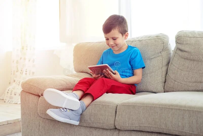 Ребенок на диване фото Side View of Small Boy Sitting on Sofa with Tablet Stock Photo - Image of caucas