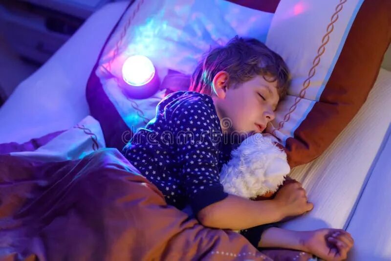 Ребенок спит ночью фото Little Preschool Kid Boy Sleeping in Bed with Colorful Lamp. School Child Dreami