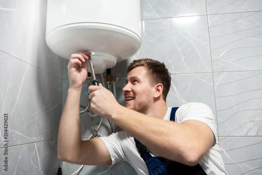 Ремонт воды фото young handsome smiling man worker in uniform repairing water heater using screwd